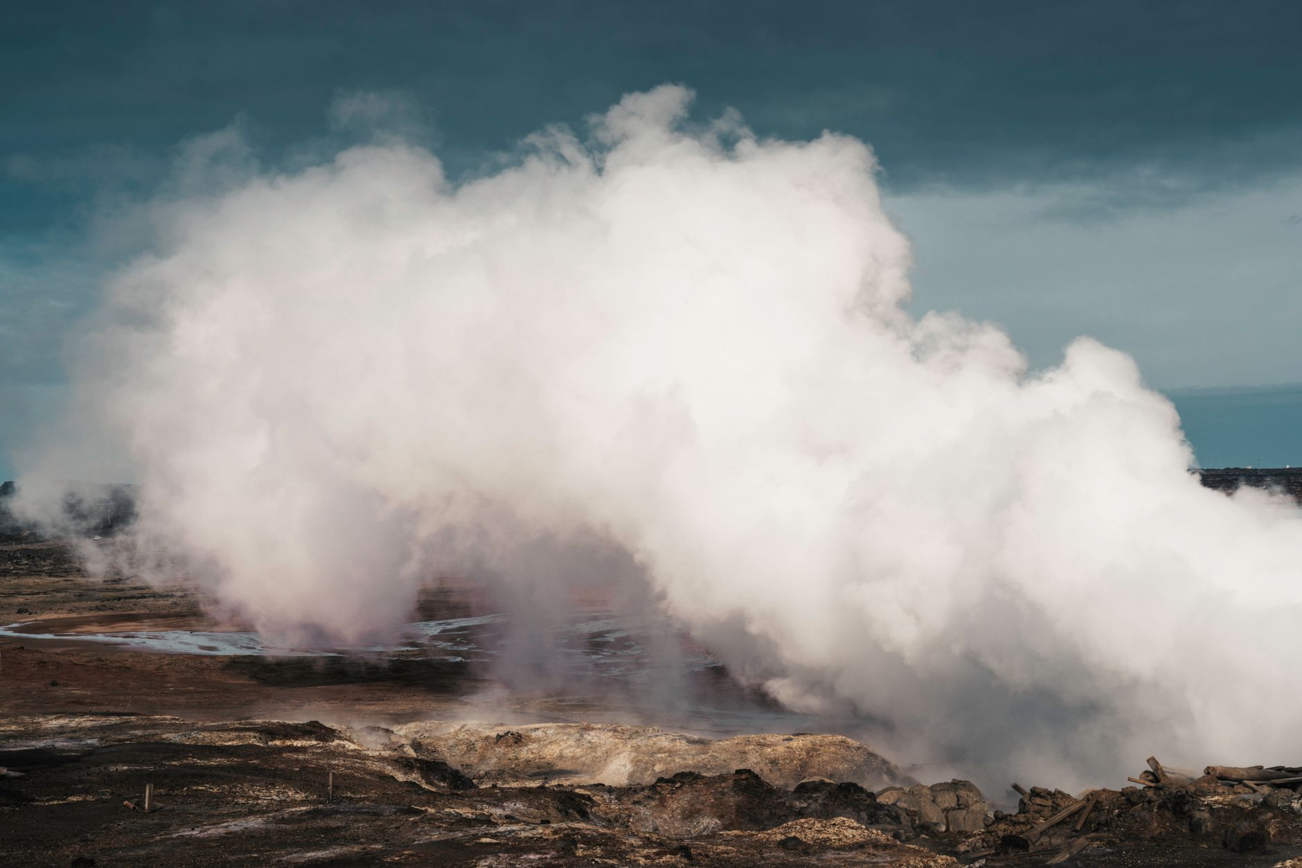 Grand panache de vapeur blanche sur un terrain volcanique rocheux, sous un ciel sombre et nuageux.